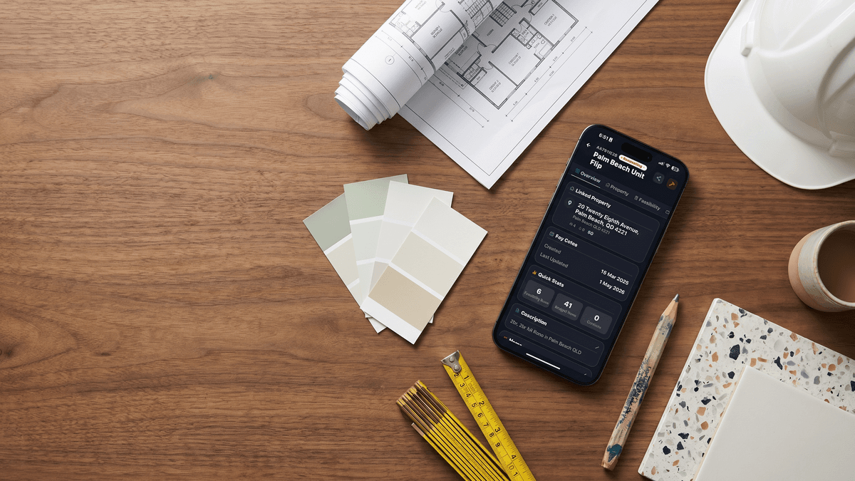 iPhone showing the FlipPro AI Palm Beach Unit Flip project overview, surrounded by floorplans, paint swatches, tile samples and a builder's pencil on a walnut workbench